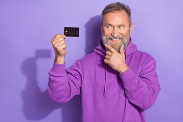 Portrait of old positive good mood cheerful man dressed purple hoodie look at black credit debit...