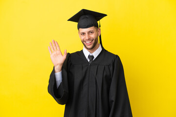 Young university graduate caucasian man isolated on yellow background saluting with hand with happy expression