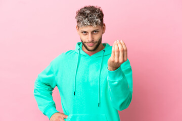 Young handsome caucasian man isolated on pink background making Italian gesture