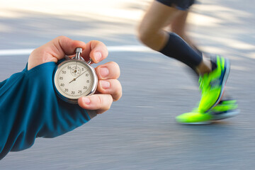 measuring the running speed of an athlete using a mechanical stopwatch. hand with a stopwatch on the background of the legs of a runner.