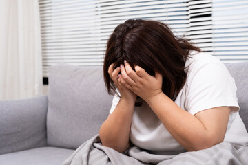 Close up shot of Young Asian girl crying while sitting on sofa inside of living of the house. Sad and stress emotion expression of chubby overweight Asian women with copy space for text.