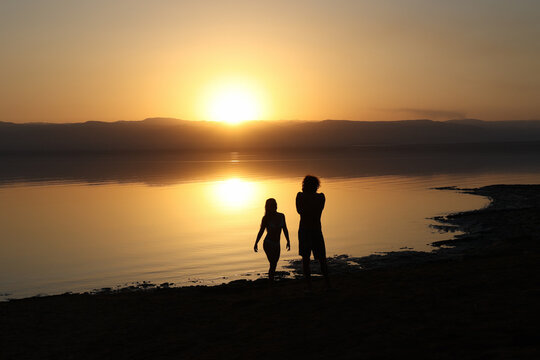 silhouette of couple taking pictures on dead sea at sunset