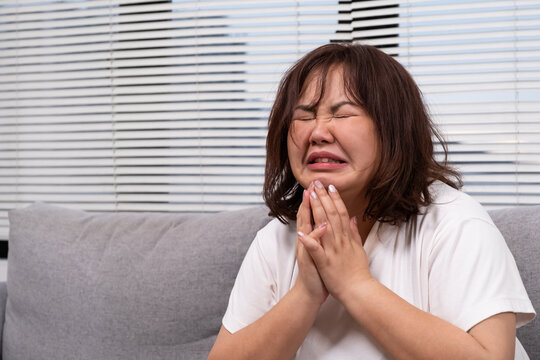 Close up shot of Young Asian girl crying while sitting on sofa inside of living of the house. Sad and stress emotion expression of chubby overweight Asian women with copy space for text.