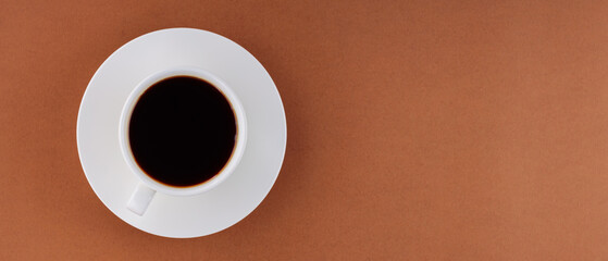 Cup with coffee on saucer on brown background. Black coffee for breakfast. Flat lay. Panoramic shot