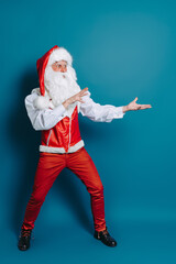 Fototapeta na wymiar Full size of stylish santa claus who gesturing hands pointing to ad text. New Year advertisement