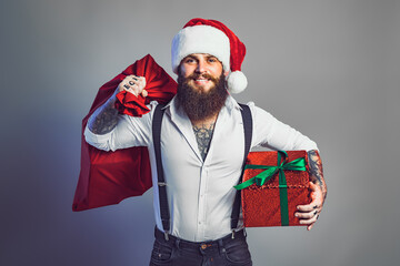 bearded smiling man in Santa's hat in white shirt holds sack and gift box. New Year concept 