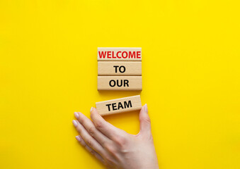 Welcome to our team symbol. Concept words Welcome to our team on wooden blocks. Beautiful yellow background. Businessman hand. Business and Welcome to our team concept. Copy space.
