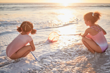 Children, girls and fishing with nets at the beach in playful fun on summer vacation in the outdoors. Little girl siblings playing and exploring the ocean in low tide to catch fish in the sunset