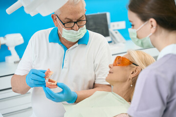 Seriously dentist in glasses with artificial jaw with braces in dental clinic