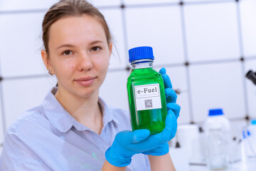 young woman holding a chemical bottle with a green liquid in her hands text on the label e-fuel...