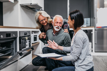 Senior husband and wife talking with saleswoman in appliances store. - 536582301
