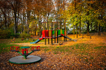 Trees with colorful autumn foliage. Children's empty playground with slides and swings is covered...