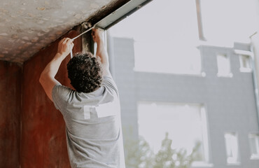 A young caucasian man is repairing a window opening, removing the silicone insulation.