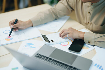 Portrait of an Asian male accountant working on a desk calculating taxes from annual financial documents using a calculator at work