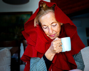 elderly lady drinking hot tea while freezing at home due to lack of heating; pensioners freezing at...