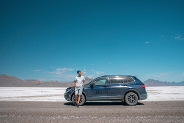 Man standing by car at Bonneville salt flat. Male tourist is relaxing at tranquil landscape with clear sky in background. He is spending leisure time at famous place during summer.