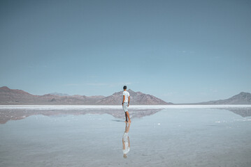 Man looking at beautiful Bonneville salt flat and mountains with clear sky in background. Tourist exploring lake with reflection during sunny day. He is enjoying summer vacation at famous place.
