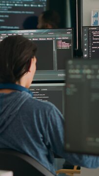 Vertical video: Database programer writing code on terminal window using multiple monitors in it agency office. System software developer typing database information, computing big data script.