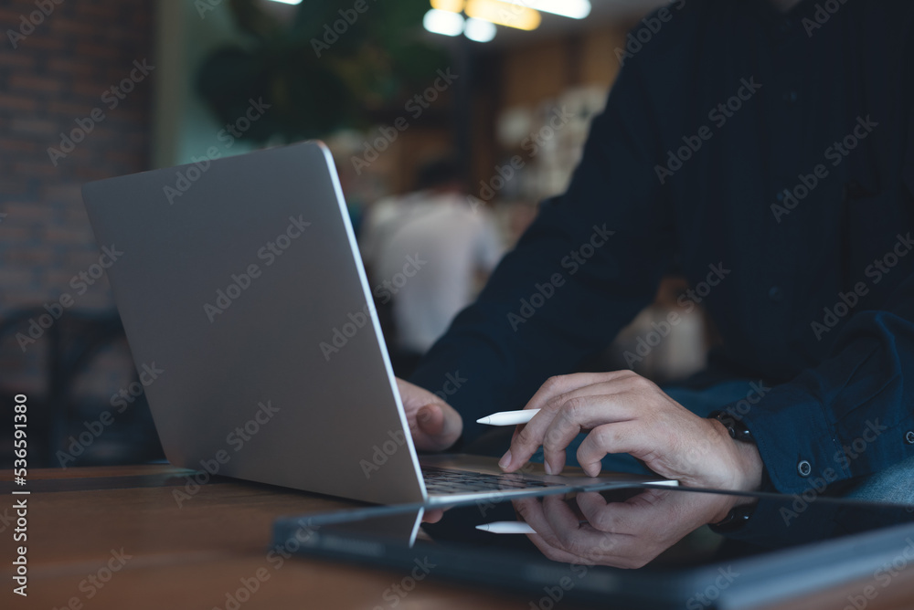 Wall mural man working on laptop computer and using digital tablet surfing the internet on wooden table at coff