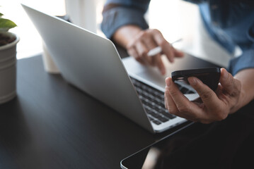 Close up of business man working on laptop computer and using mobile phone with digital tablet on office table