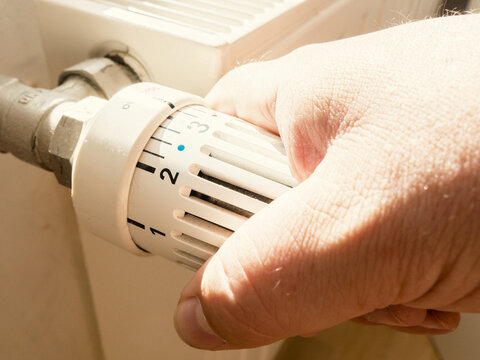 Main d'homme baissant le thermostat de son chauffage radiateur - Personne qui r&egrave;gle la temp&eacute;rature de son logement pour faire des &eacute;conomies, &agrave; cause de l'augmentation des prix de l'&eacute;nergie et du gaz