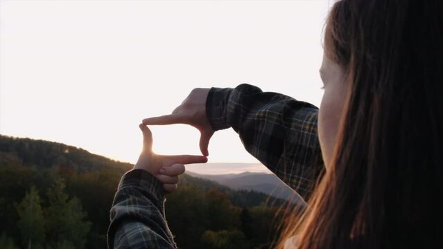 Business planning, strategy and vision concept. Close-up side view of young female making frame gesture with amazing sunset in mountains. Woman capturing sunrise. Copy space for promotion content