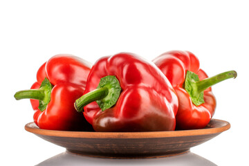 Three red organic, bell peppers in a clay plate, close-up, isolated on white.