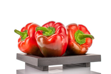 Three red organic, bell peppers on a wooden tray, close-up, isolated on white.