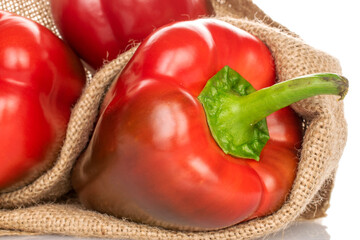 Three red organic, bell peppers in a jute bag, close-up, isolated on white.