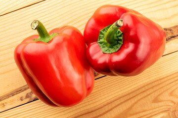 Two juicy red sweet peppers on a wooden table, close-up, top view.