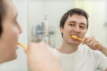 young man brushes his teeth in front of a mirror in the bathroom. oral hygiene, dental care