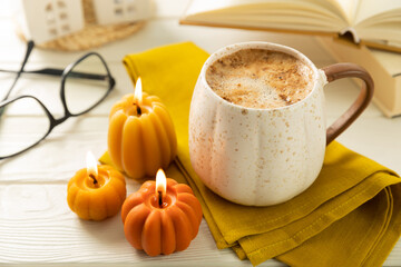 Autumn composition, hot cup of coffee, candles, candlesticks miniature house on a wooden table. Seasonal, morning hot coffee. Relaxing and still life concept. Cozy interior decor.