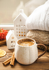 Obraz na płótnie Canvas Autumn composition, a hot cup of coffee, candles, candlesticks, a miniature house and a warm sweater on a wooden table.Seasonal, morning hot coffee. Relaxing and still life concept.Cozy interior decor