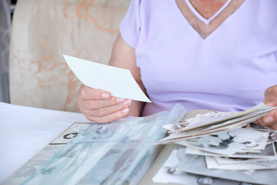 elderly woman holding album with black and white retro photographs. Senior woman is looking her own old photos at home. woman has got smile while remembering how young she was.