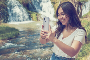 Joven mujer haciendo selfie en la naturaleza con río y cascadas