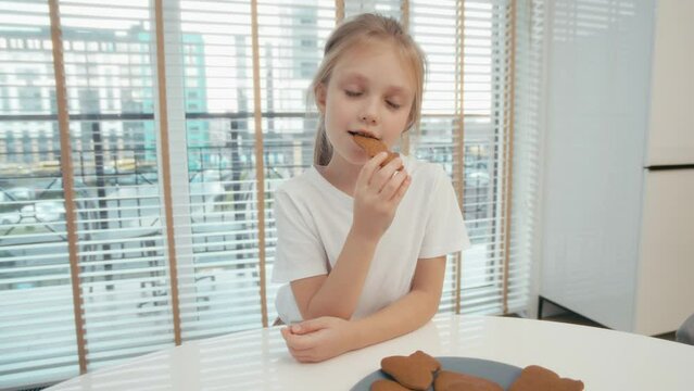 Adorable child eating traditional Christmas cookie while stand at the table and watch TV. Chid takes a gingerbread cookie, tasty Christmas sweets in shape of mustache and bit it