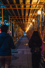 two women walking down sidewalk with scaffolding and construction lights