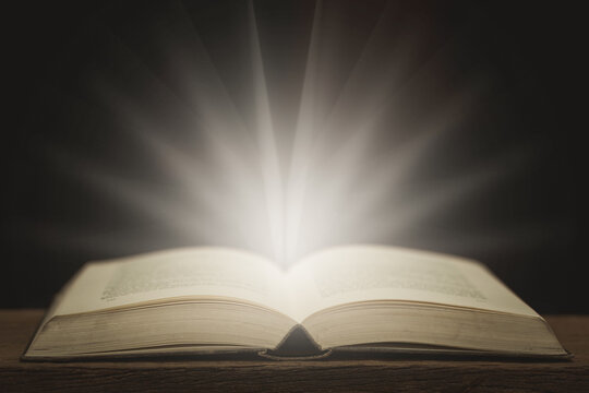 Picture of an antique book open on a wooden table with vintage fairlights and dark style background.
