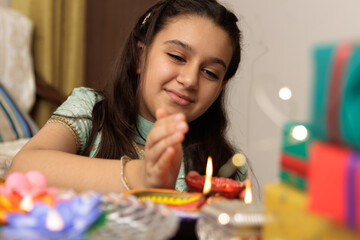 Young girl, kid, dressed up in ethnic lighting diya or lamp with smile expression pose for photo with family in background celebrating diwali Hindu festival Laxmi poojan