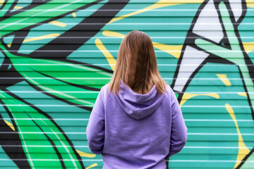 Young blonde woman in purple violet hoodie from back on green modern background copy space mockup...