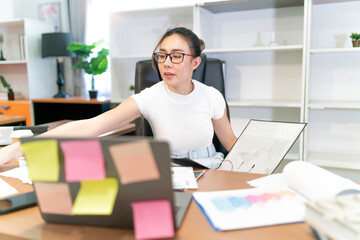 asian beautiful woman focus on business work. overtime glasses female worker looking at file for document to done work. workplace full with sheet paper and sticky notes by motivation occupation girl
