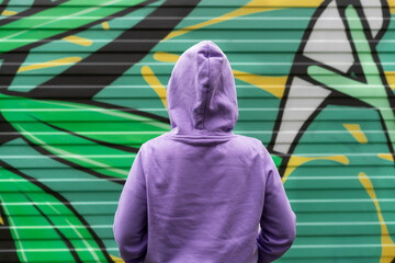 Young woman in hood in purple violet hoodie from back on green modern background copy space mockup...