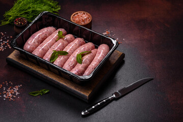 Raw sausages with ingredients on a cutting board on a dark concrete background with copy space