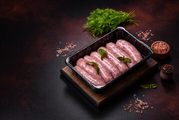 Raw sausages with ingredients on a cutting board on a dark concrete background with copy space