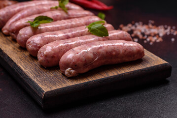 Raw sausages with ingredients on a cutting board on a dark concrete background with copy space