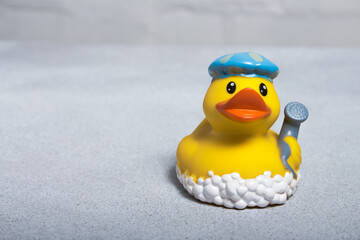Yellow rubber duck for a bath in a bath cap and with a shower head in the wing on a light background