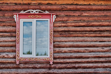 Window with carved wooden architraves. Log facade of typical rural house of Buryatia, Russia.
