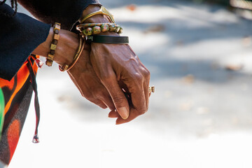 the hands of an African American woman with sister locs in her hair wearing several stone and copper bracelets and a green ring with fallen autumn leaves on the ground at Atlanta Botanical Garden