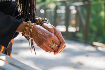 the hands of an African American woman with sister locs in her hair wearing several stone and copper bracelets and a green ring with fallen autumn leaves on the ground at Atlanta Botanical Garden