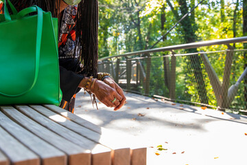 the hands of an African American woman with sister locs in her hair wearing several stone and copper bracelets and a green ring with fallen autumn leaves on the ground at Atlanta Botanical Garden